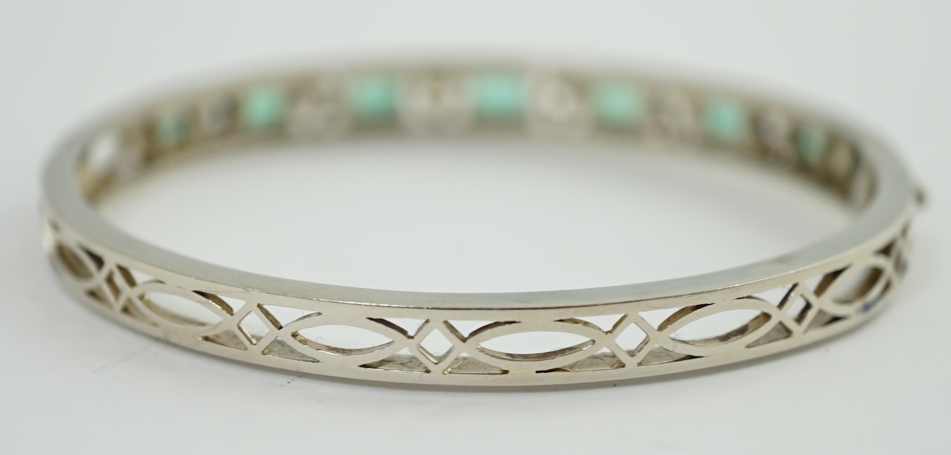 A modern 14k white gold, seven stone graduated emerald and six stone round cut diamond set hinged bangle